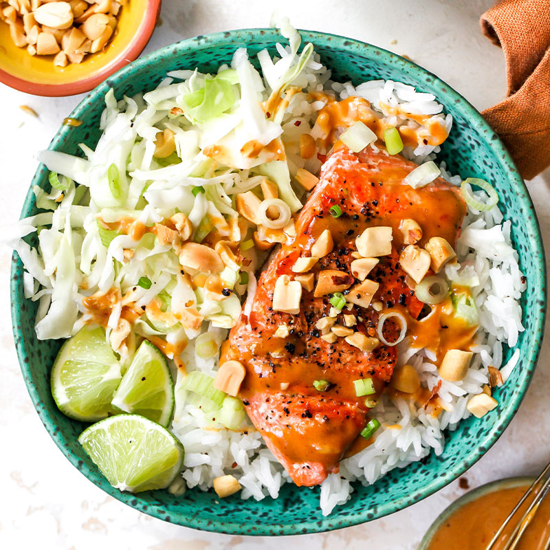 Overhead shot of a big piece of firecracker salmon on a bed of rice with garnish and lime wedges.