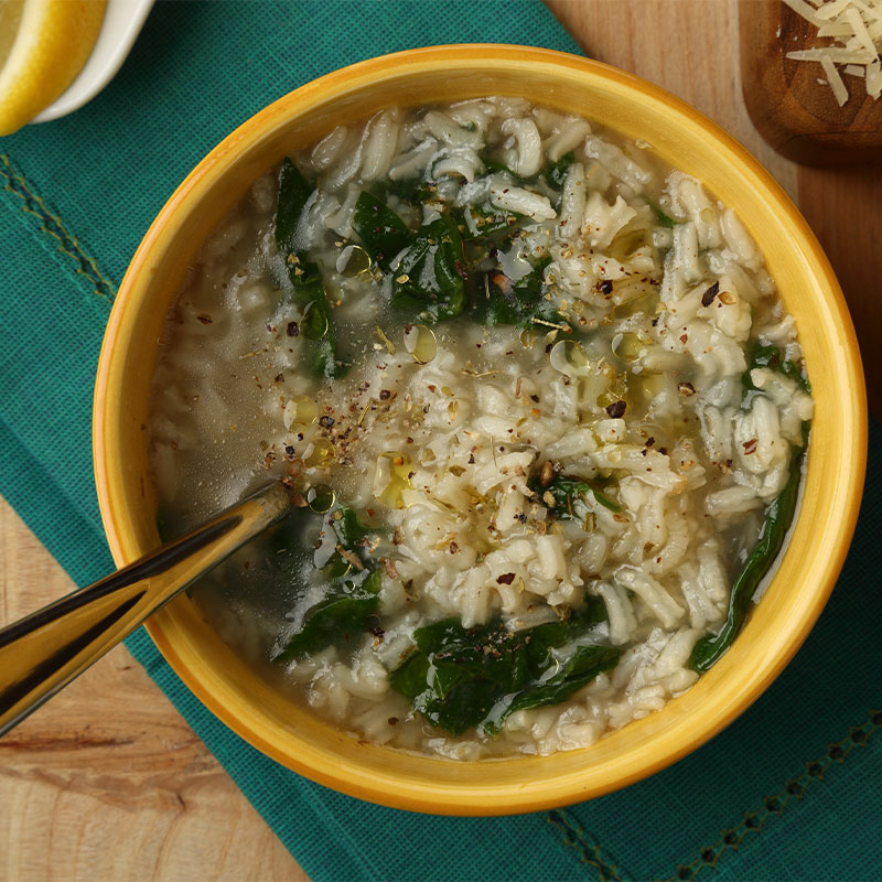 Overhead shot of a bowl full of spinach-rice soup with spinach leaves and rice grains exposed.