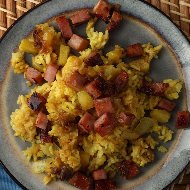 Overhead view of cubed ham and pineapple pieces sit on top of a bed of yellow rice.
