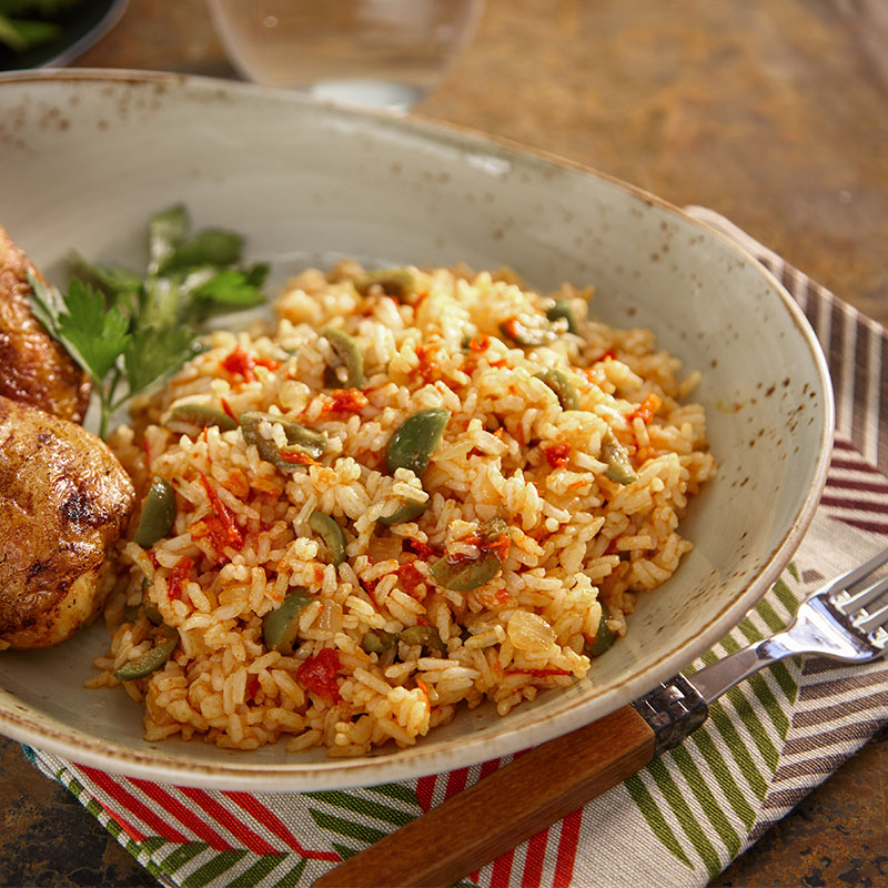 Side view of harissa mixed rice with chicken on a cream plate.