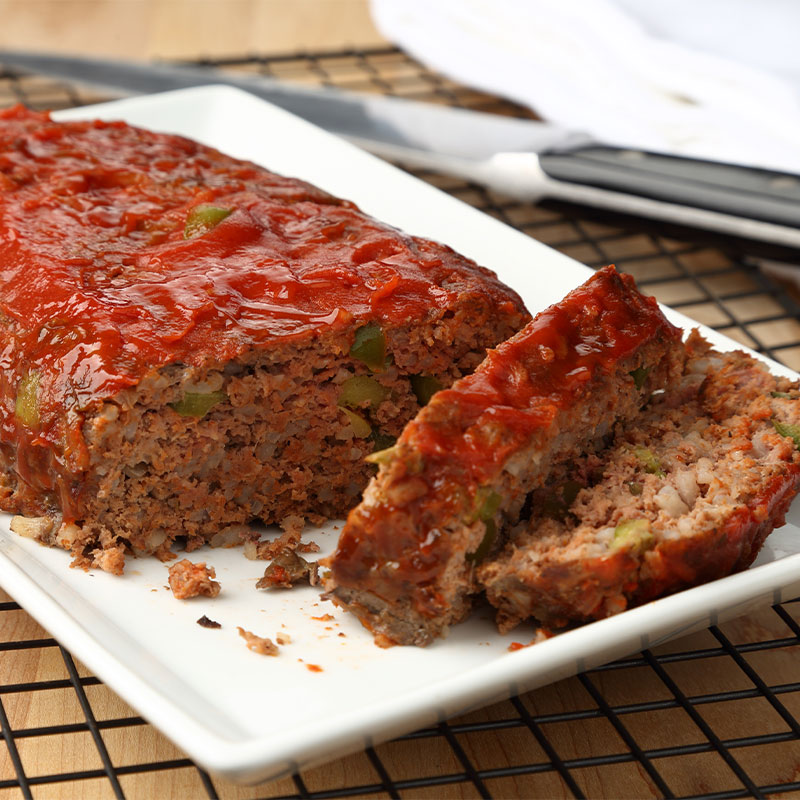 Two slices of Homestyle Meatloaf sit next to the remaining intact meatloaf on a white serving platter.