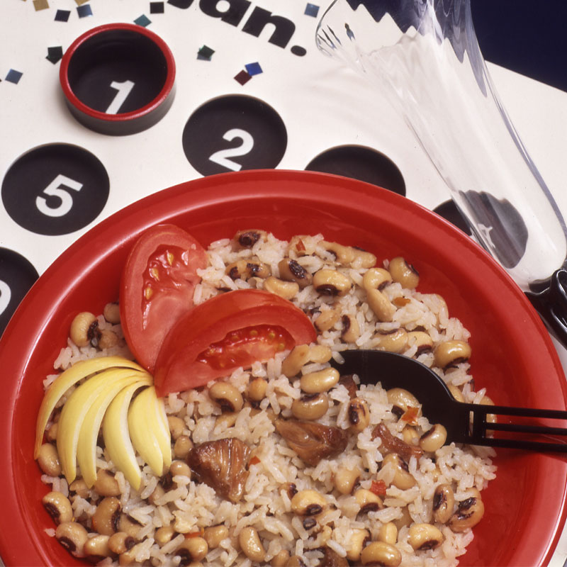 Hoppin John Overhead shot of a red bowl full of Hoppin’ John with tomato slices on top.