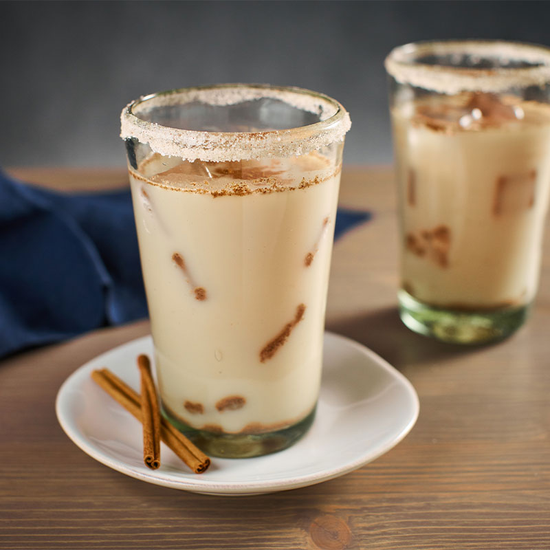 Side view of two glasses filled with Horchata with cinnamon sticks in view.