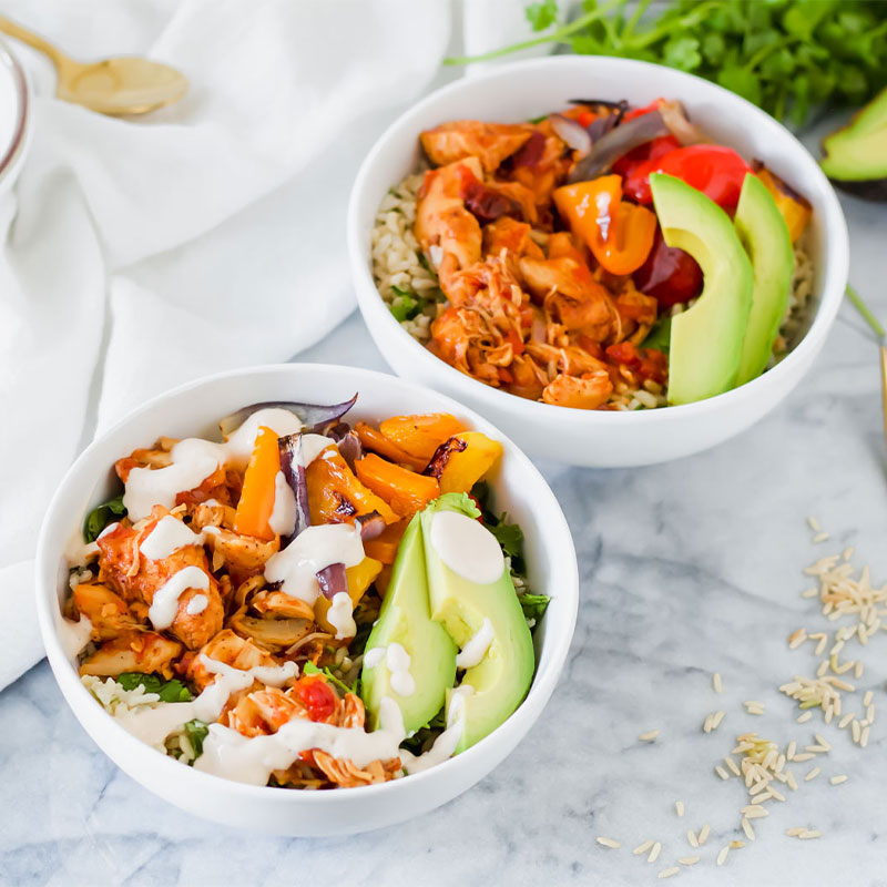 Overhead shot of two chipotle chicken rice bowls topped with veggies and a drizzled white sauce.