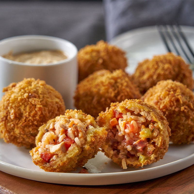 Side shot of a plate full of 6 Jambalaya Arancini balls with dipping sauce to the side 
