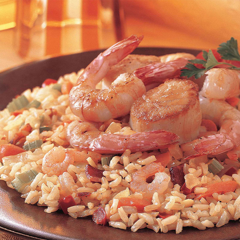A serving of Jeweled Seafood Rice topped with five shrimp and a scallion on a brown plate.