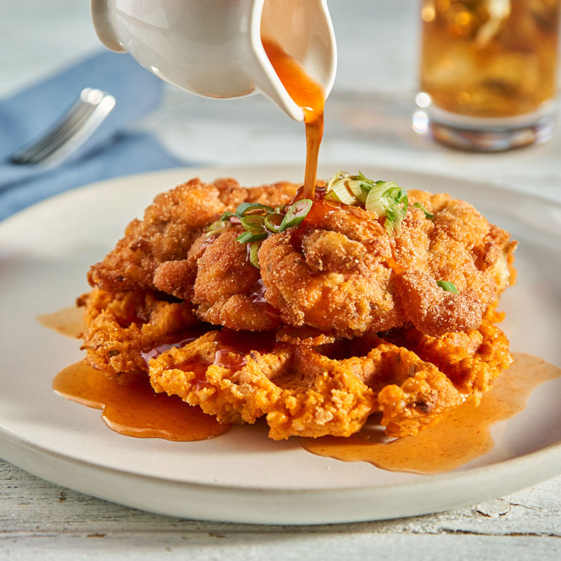 Side view of Korean fried chicken on top of a rice waffle on a white plate.