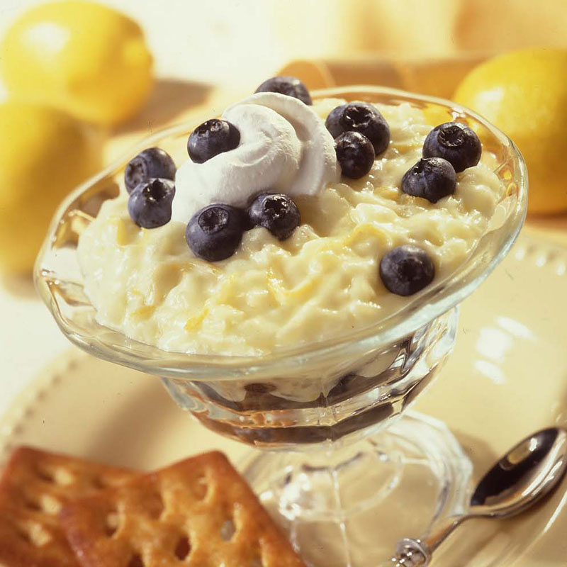 Side view of lemon blueberry rice pudding topped with whipped cream and blueberries in a glass dish.