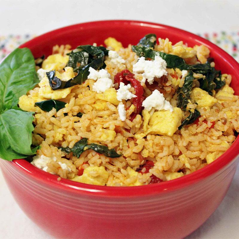 Mediterranean Breakfast Kale Rice Bowl A serving of Mediterranean Breakfast Kale Rice in a red bowl and garnished with basil.
