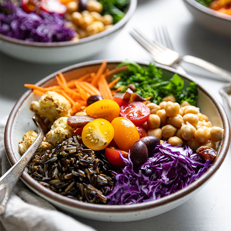 Side view of a Mediterranean Wild Rice Bowl topped with an assortment of colorful vegetables. 