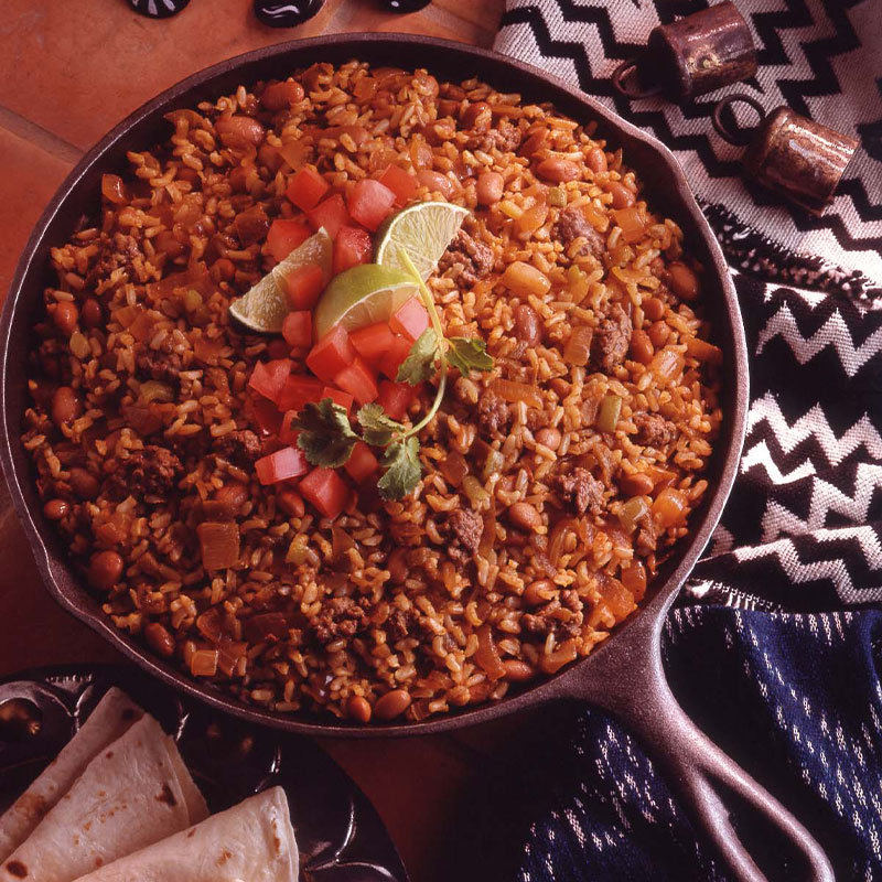 Mexican Skillet Rice Overhead shot of a skillet full of Mexican Rice and topped with cilantro, diced tomatoes, and limes wedges.