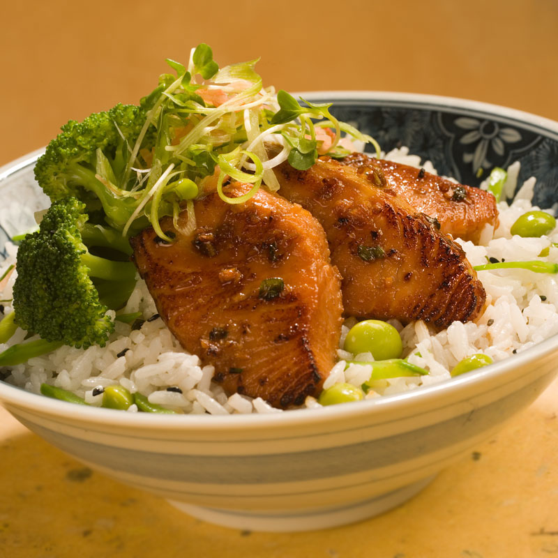 Close up view of miso and soy glazed salmon over rice with broccoli and edamame in a bowl.