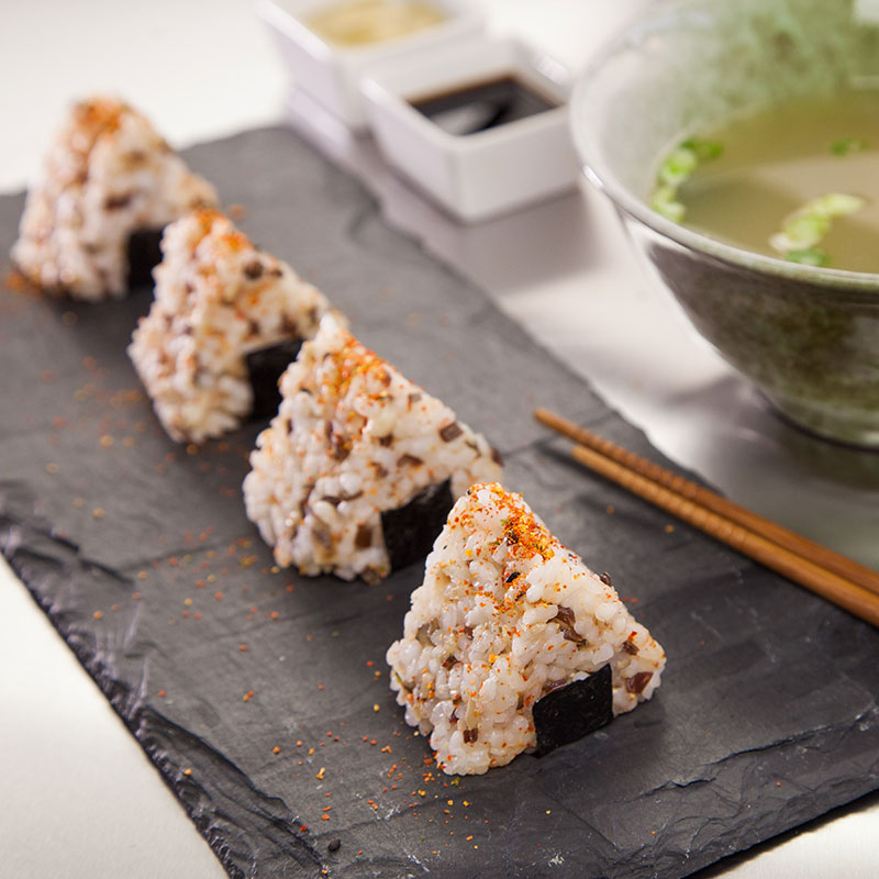 Side view of onigiri on a slate serving platter with miso soup on the side.