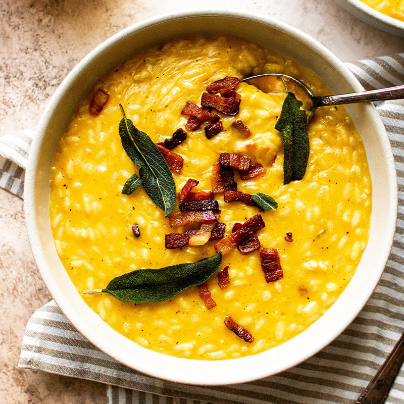 Overhead view of a white bowl full of Pumpkin Risotto with Bacon, Gouda, and Sage.