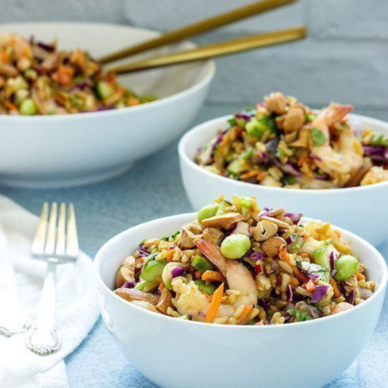 Side view of rainbow Asian rice and shrimp salad in a white bowl.