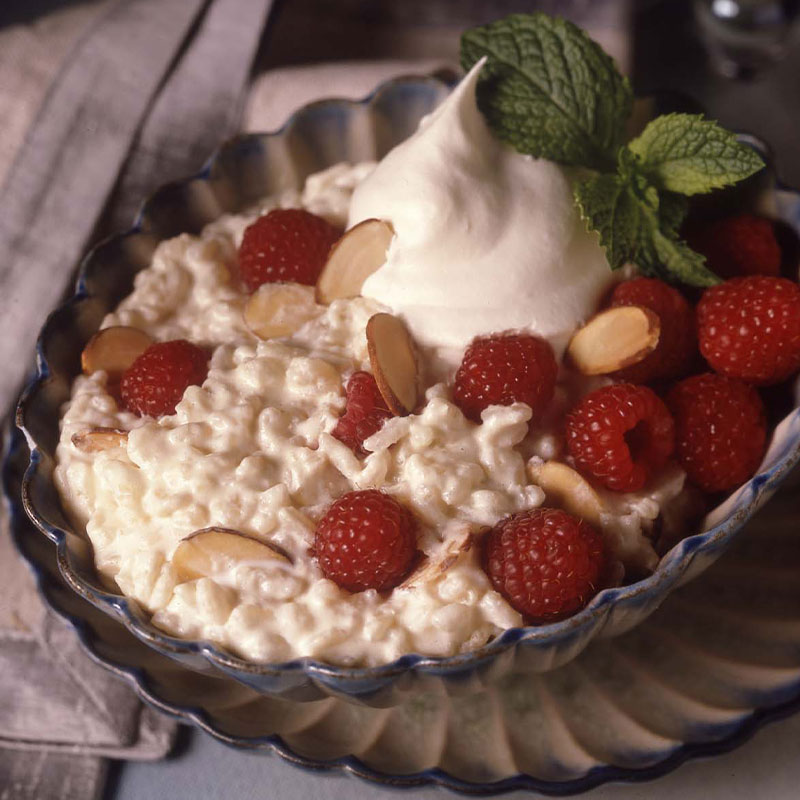 Raspberry Rice Pudding topped with Raspberries, sliced almonds, whipped cream, and basil in a bowl.