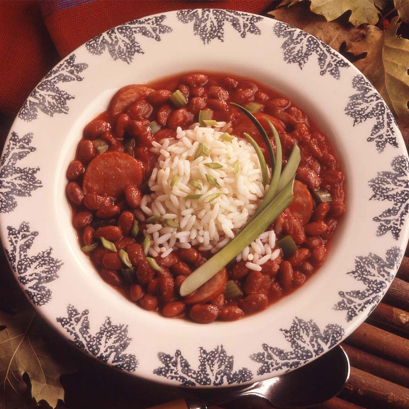 Overhead shot of a cup of white long grain rice on top of and surrounded by red beans and sausage.