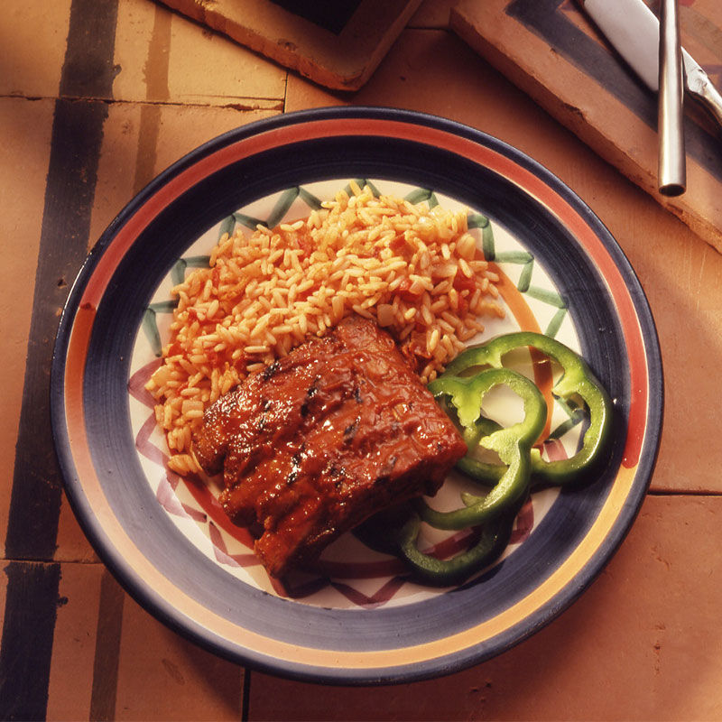 Overhead shot of a serving of red rice plated with ribs and green peppers.