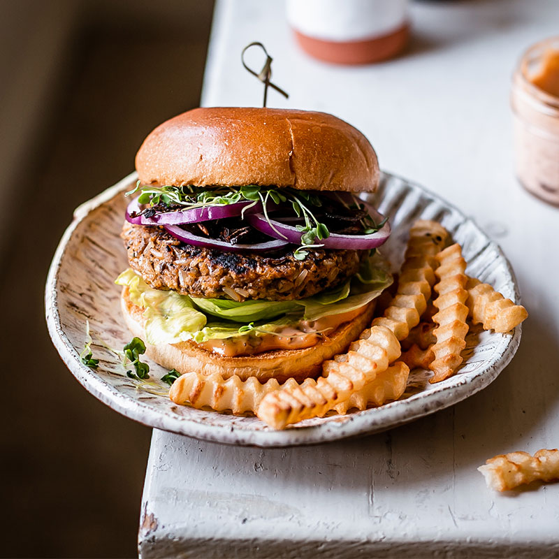 A plated Rice Burger with Sweet Potato and Mushroom with a side of fries on the corner of the table.