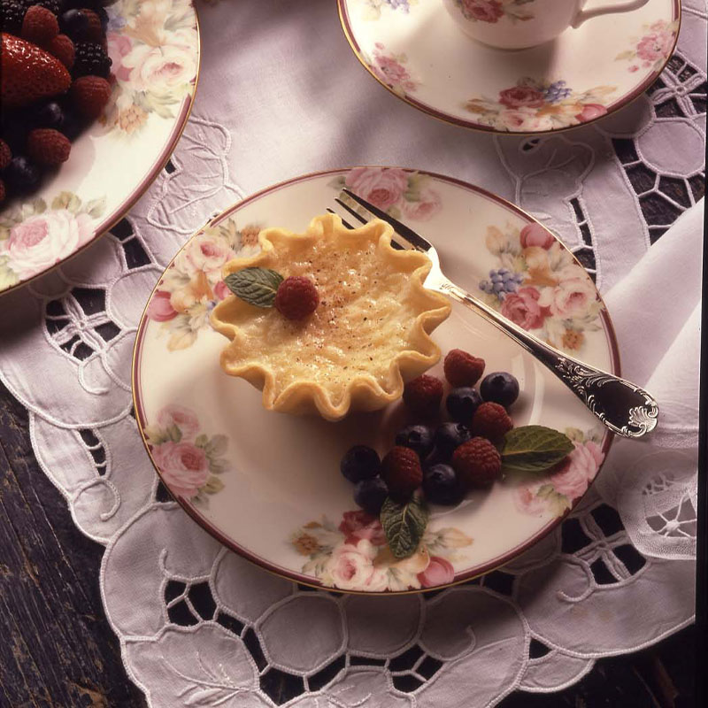 A single Rice Pudding Tart on a fancy plate with a side of berries.   