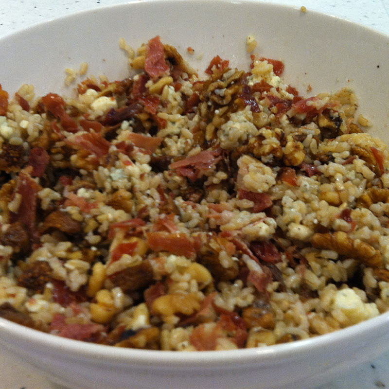 Close up view of rice salad with prosciutto, figs, gorgonzola and walnuts in a white serving bowl.