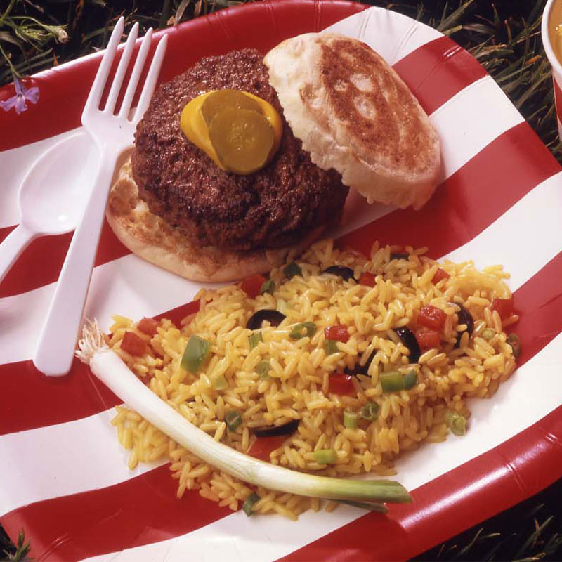 Overhead view of saffron rice salad served with a hamburger on a paper plate.