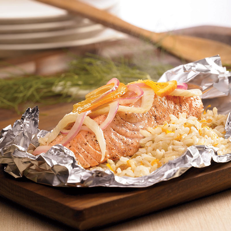 Side view of salmon and rice packets with fennel, orange, and raisins on a wood platter.