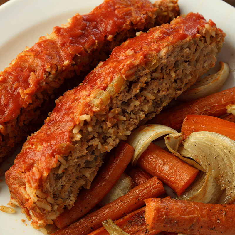 Two slices of Rice Meatloaf on top of roasted carrots and onions.