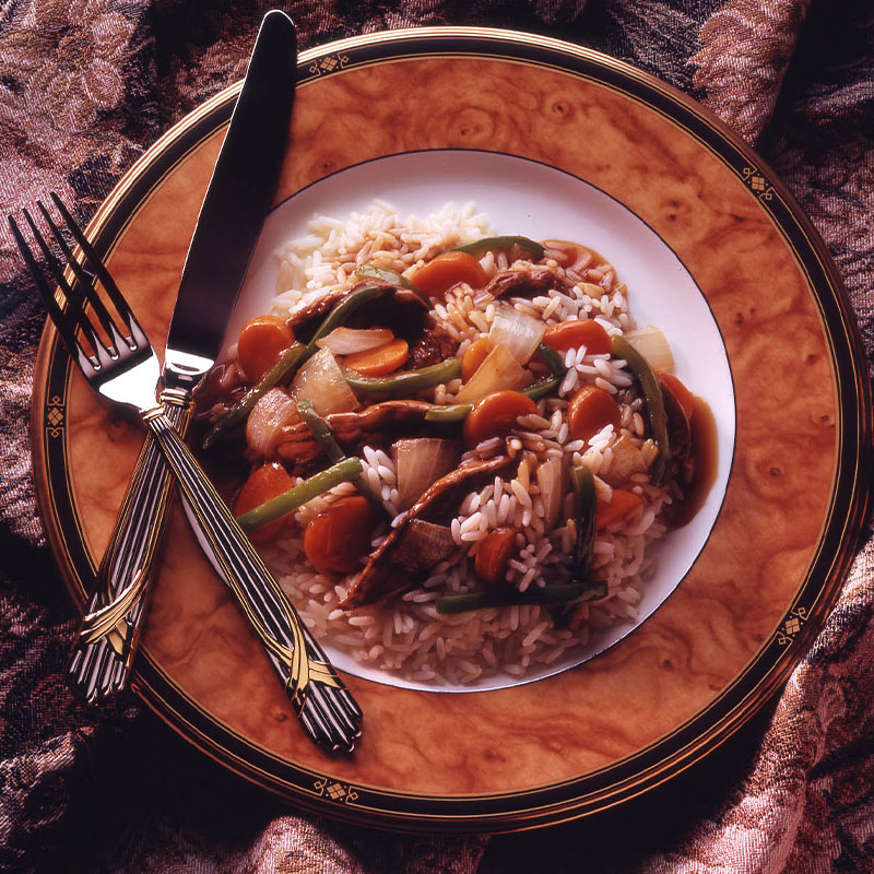 Overhead image of Sherried Beef on top a bed of white rice with silverware to the side.