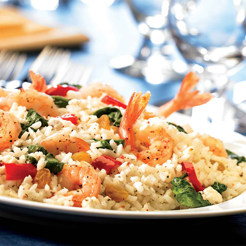 Side view of a plate of Shrimp and Creamy Spinach Feta Rice with shrimp tails sticking out.