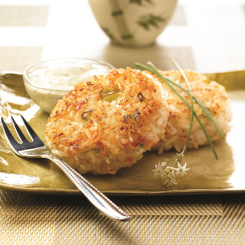 Two Shrimp and Rice Patties on a plate with Creamy Cilantro Sauce in the background.