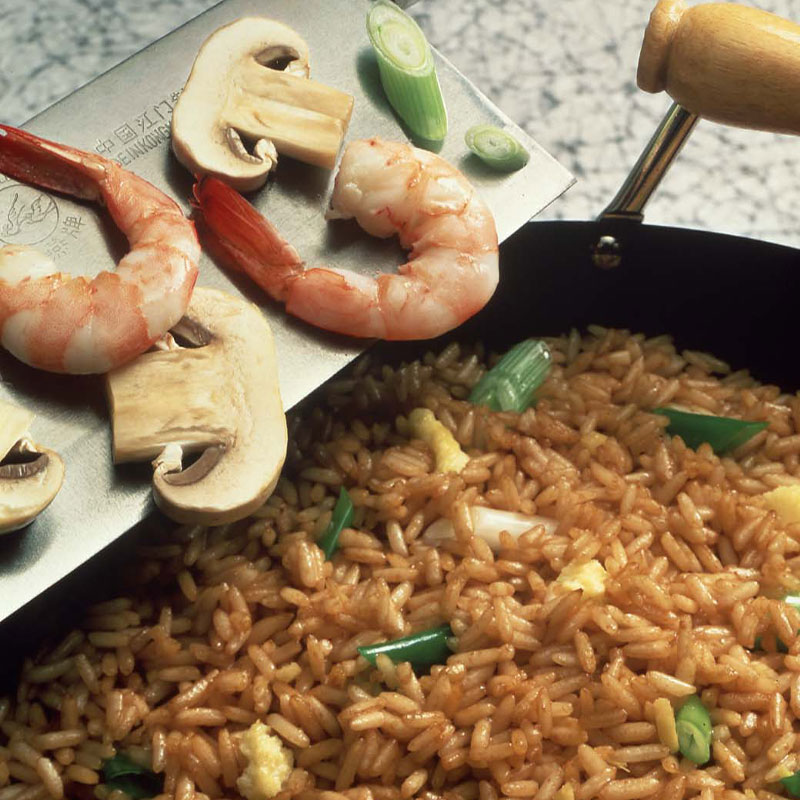 Overhead view of fried rice in a wok with shrimp, mushrooms, and green onion being added to the wok.