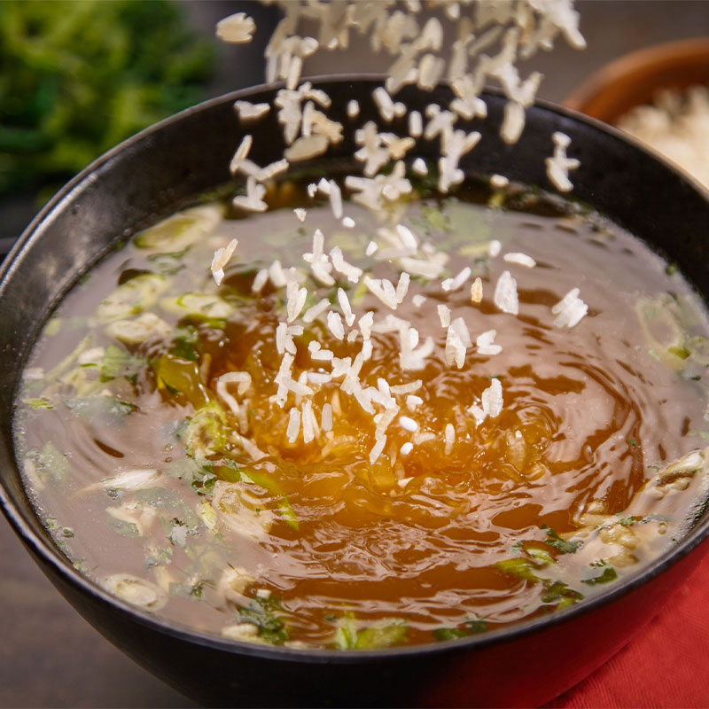 Overhead shot of soup in a bowl as grains of rice are poured in.