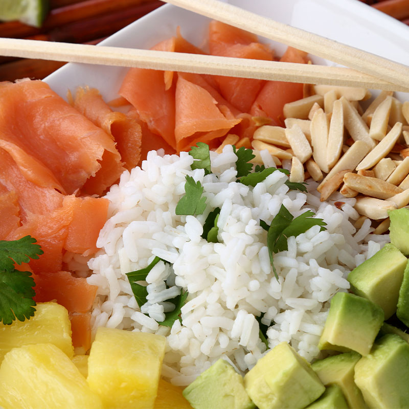 Overhead shot of a neatly arranged Smoked Salmon and Avocado Breakfast Rice Bowl with ginger and pineapple chunks.