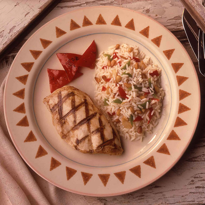 Southwestern Garlic Rice and Pine Nuts Overhead view of southwestern garlic rice with pine nuts on a white plate with grilled chicken.