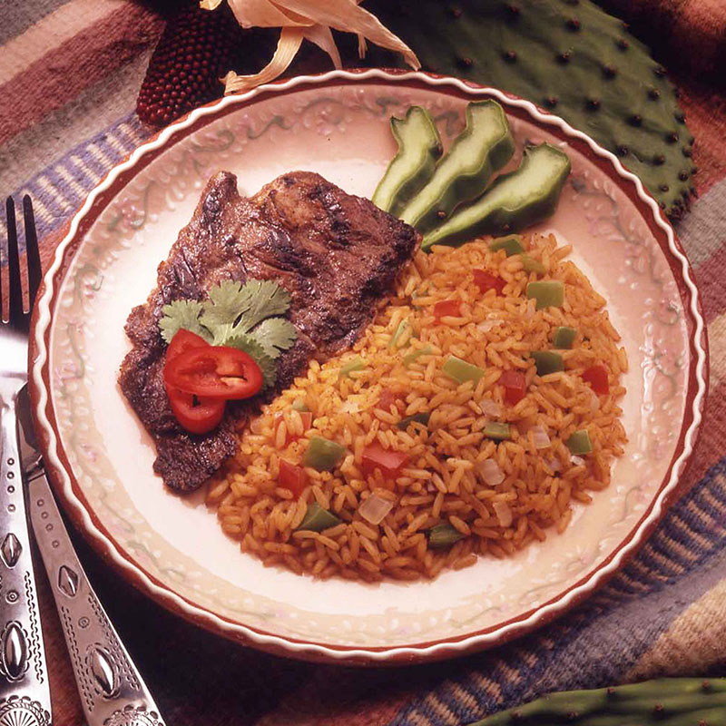 Overhead view of southwestern vegetable rice on a white plate with grilled meat.