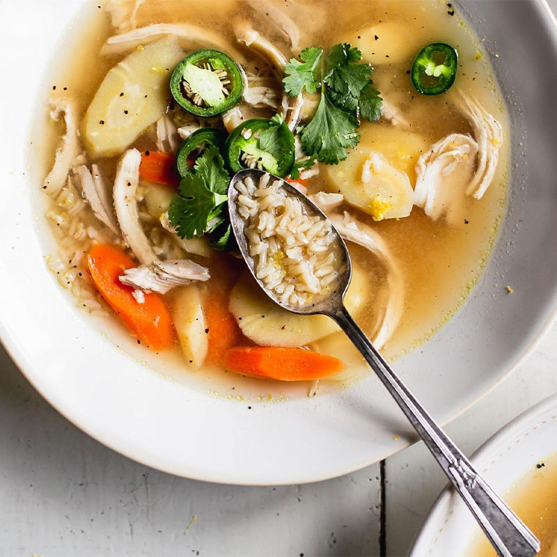 Overhead view of a bowl of Spicy Bone Broth, Chicken & Rice Soup with a spoon full of the rice soup on top