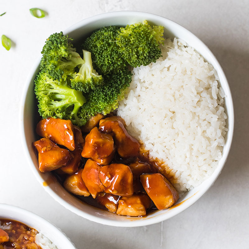 Overhead shot of a white bowl filled with white rice, spicy honey chicken pieces, and broccoli.