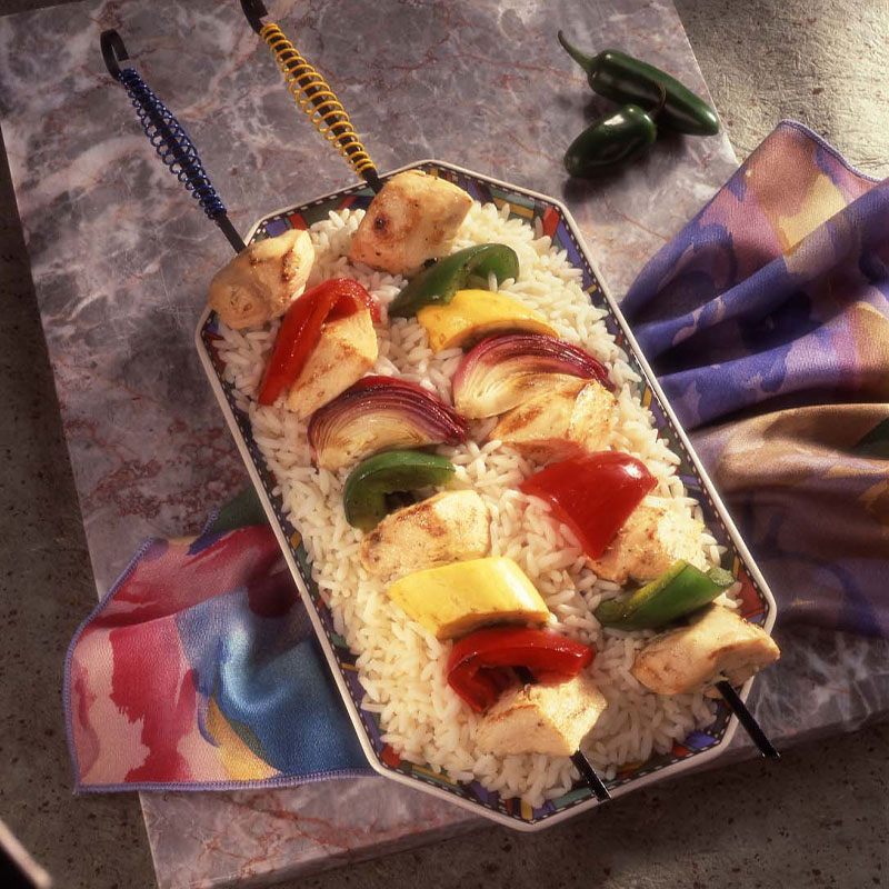 Spicy Kebabs with Rice Two Kebab sticks with grilled chicken and vegetables on a bed of white rice.