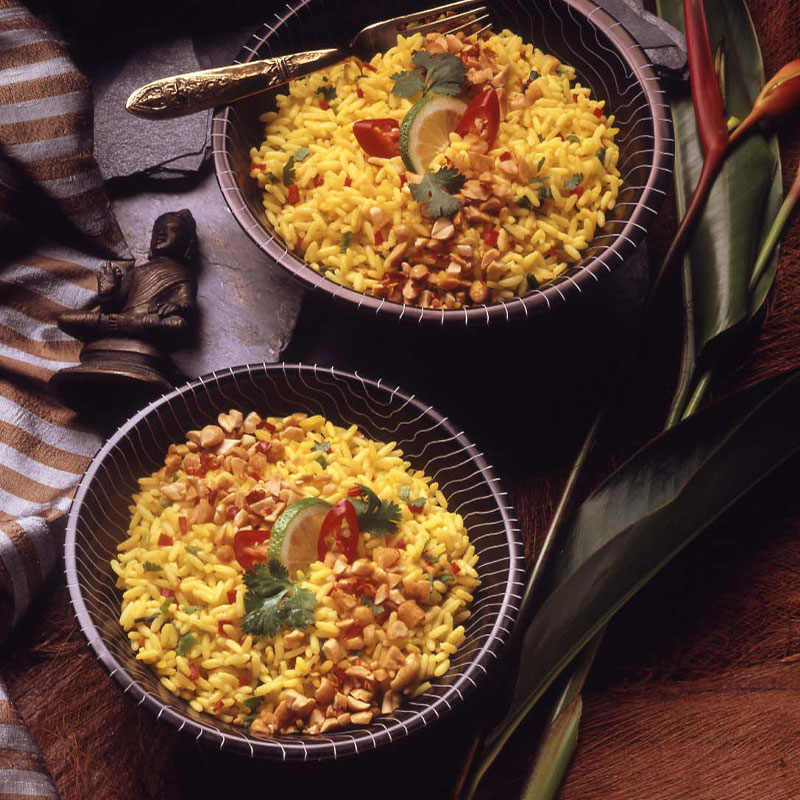 Overhead shot of two black bowls filled with Spicy Thai Rice and topped with tomatoes and a lime wedge.