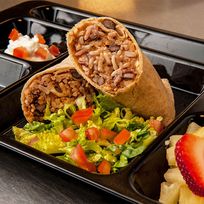 Two stuffed beef burritos stacked on top of each other and on a black cafeteria tray. 
