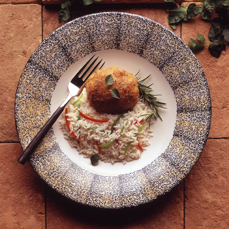 Overhead shot of a breaded chicken breast next to a bed of white rice with sliced peppers on a plate.