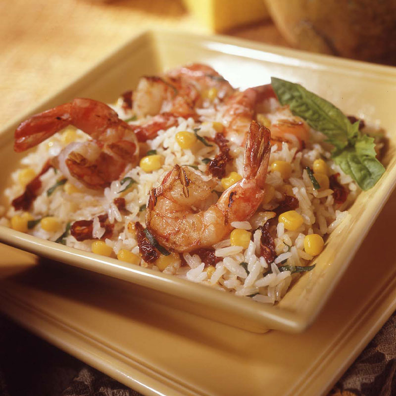 In a square bowl a bed of white rice with corn is topped with shrimp. 