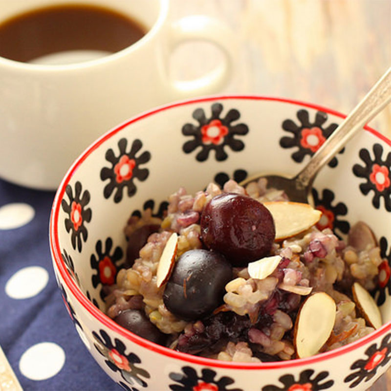 A serving of Sweet Cherry Almond Breakfast Risotto in a coffee cup with a cup of coffee in the distance.