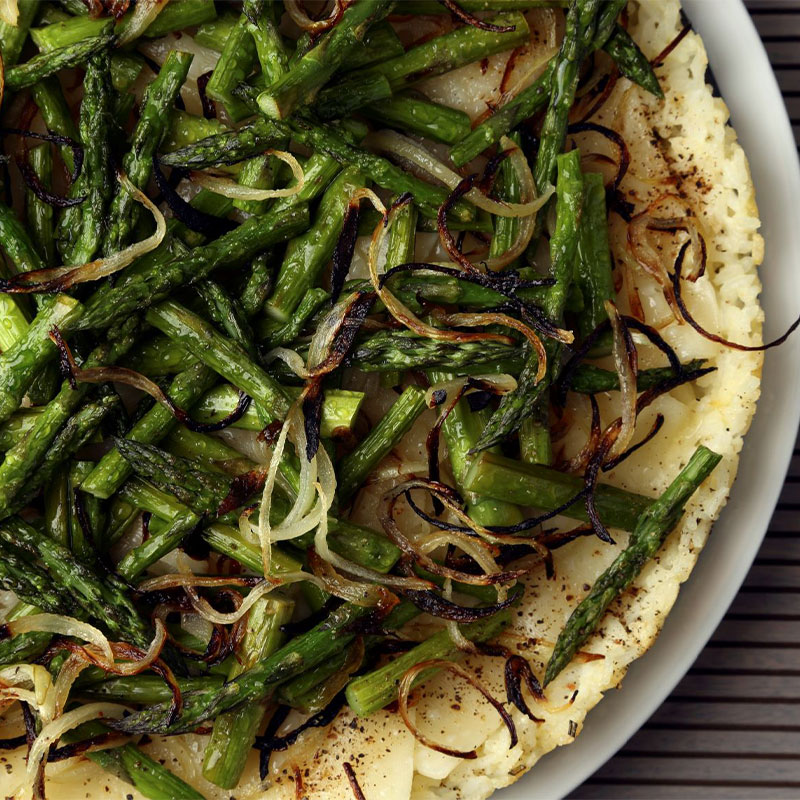 Swiss & Asparagus Rice Tart Overhead shot of a complete Swiss & Asparagus Rice Tart topped with asparagus halves and onion.