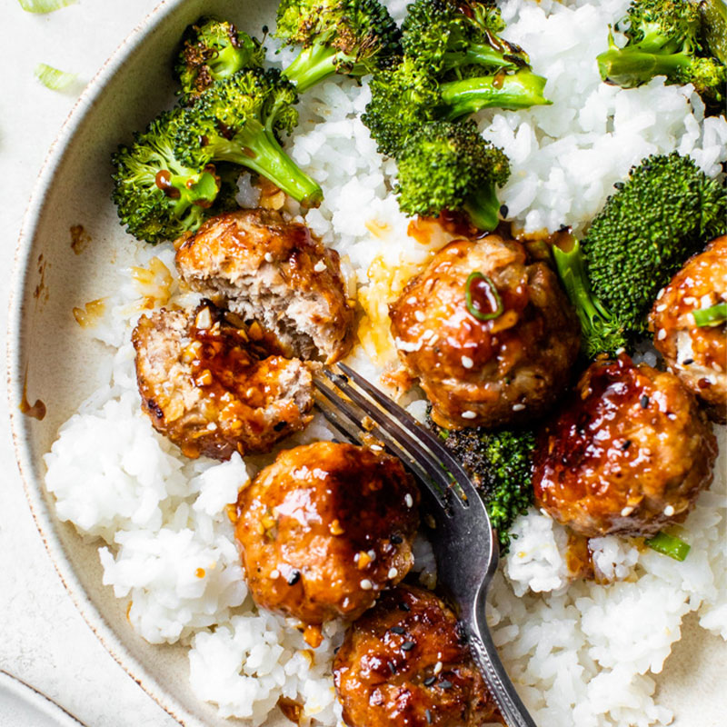 Overhead image on five teriyaki meatballs on a bed of white Jasmine rice with broccoli. 