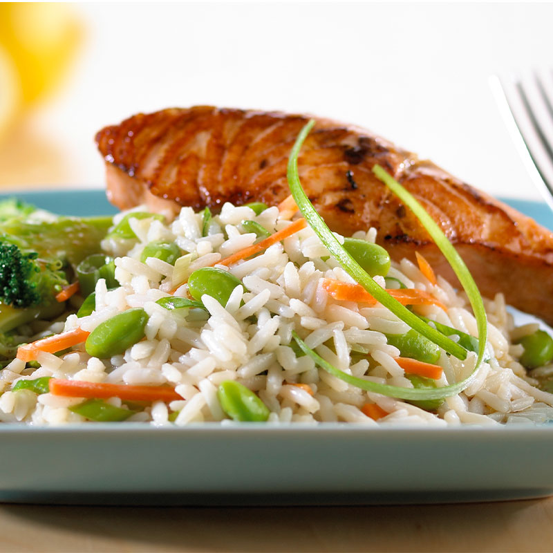 Teriyaki Salmon with Gingered Vegetable Rice Closeup shot of a portion of gingered vegetable rice with a salmon filet behind and broccoli to the side.