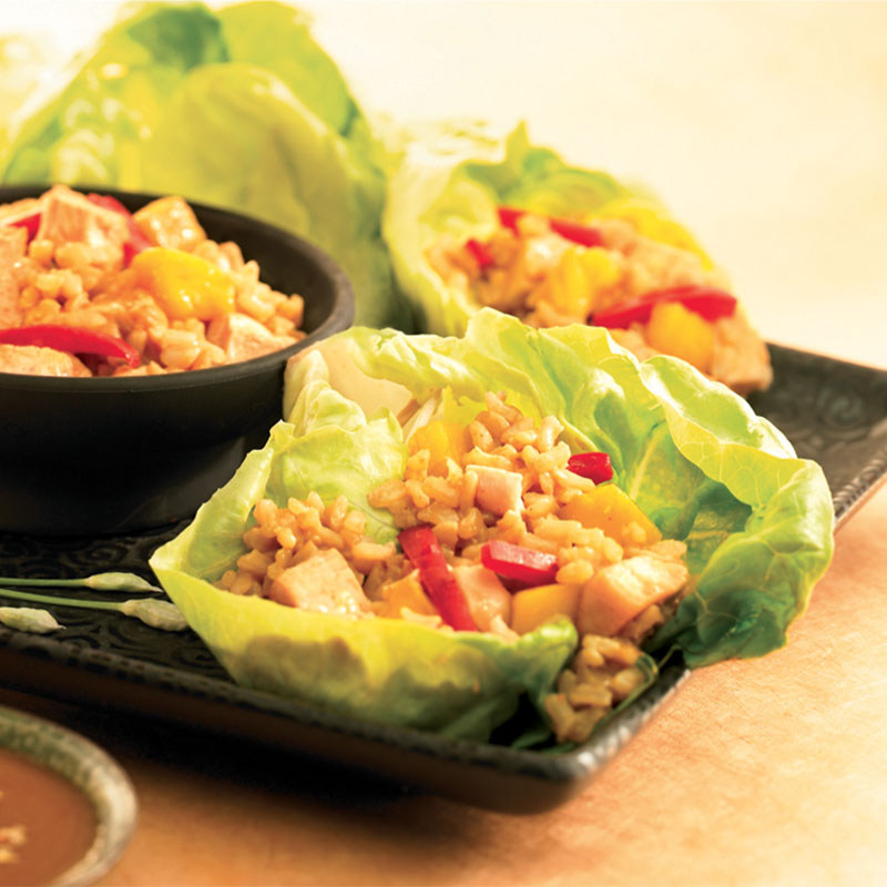 Thai Chicken and Rice Lettuce Wraps Two lettuce leaves filled with Thai Chicken and Brown Rice next to a black bowl filled with the chicken and rice.