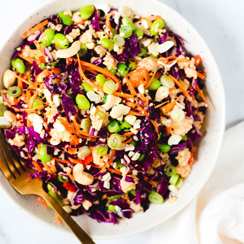 Overhead shot of a rice salad filled with peanuts, edamame, carrots slices, red cabbage, and green onion in a bowl.