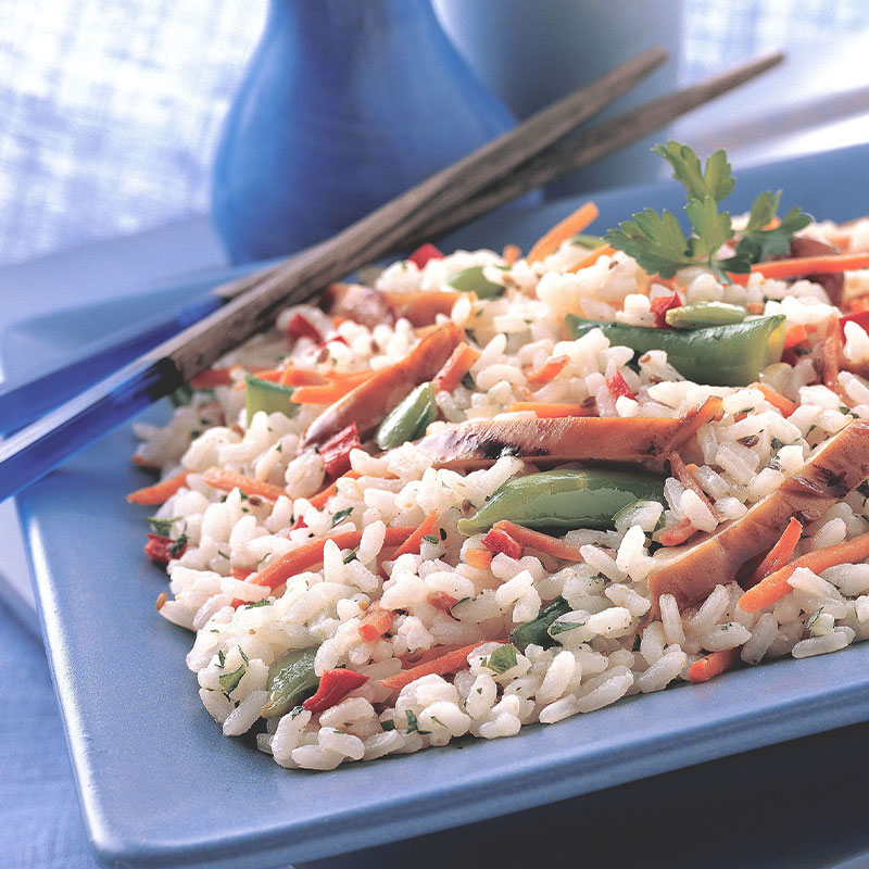Side view of a white rice mix with vegetables and chicken slices in a blue serving dish.  